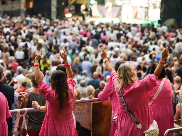 Eine Gruppe Frauen ist mit rosa Oberteilen angezogen und tanzt und feiert.