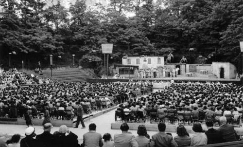 Schwarz-Weiß-Foto der Freilichtbühne von 1954 - Menschen in Anzug und Kleid sitzen vor der Bühne und lauschen einem Konzert