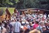 Viele Menschen holen sich an den Holzhäusern im Gastro-Bereich der BÜRGER Freilichtbühne etwas zu essen oder zu trinken.