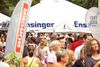Menschen stehen im Gastro-Bereich der BÜRGER Freilichtbühne unter großen Sonnenschirmen und essen oder trinken etwas.