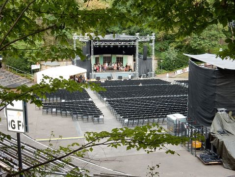 Blick von oben auf die bestuhlte Freilichtbühne - auf der Bühne übt ein Orchester